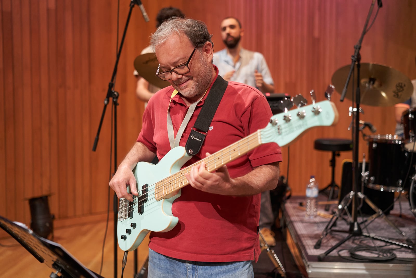 Adulto a tocar baixo numa aula d'Os Músicos, concentrado e sorridente