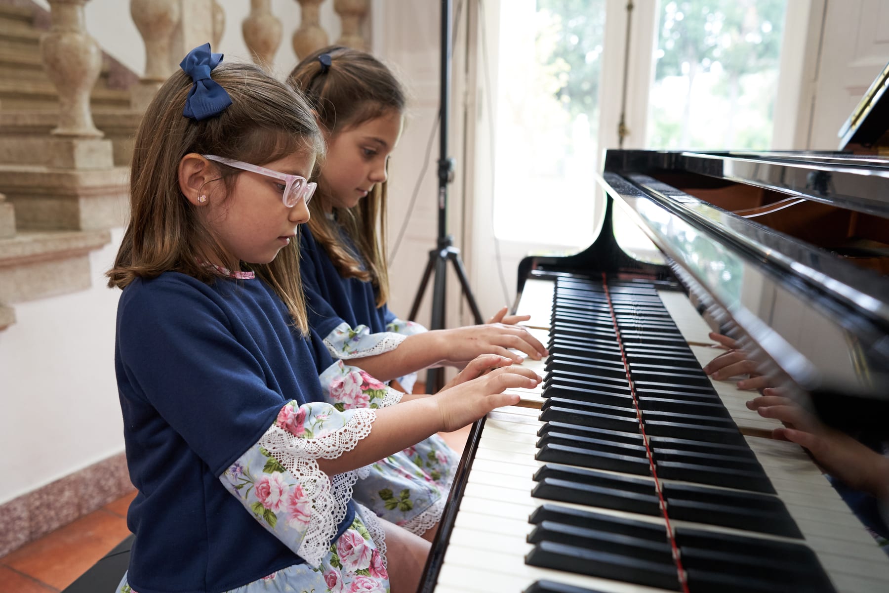 Aluno a estudar piano em casa, com um adulto por perto sem intervir